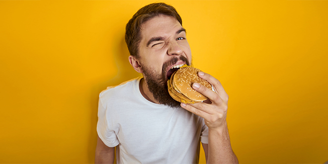 Гладан мушкарац једе хамбургер Гладан мушкарац једе хамбургер