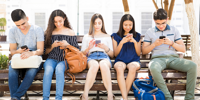 Тинејџери седе на клупи и дописују се преко мобилних телефона