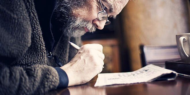 Старији мушкарац решава укрштеницу у новинама