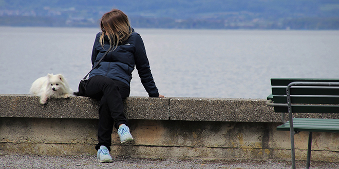 Девојка седи поред језера са својим псом