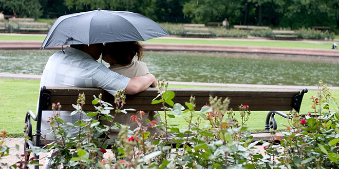 Брачни пар седи на клупи и држи кишобран